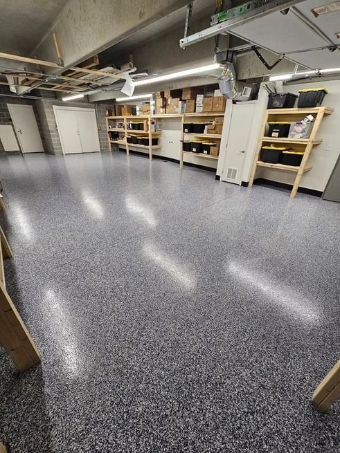 Garage with a speckled epoxy floor, shelving, and closed doors.