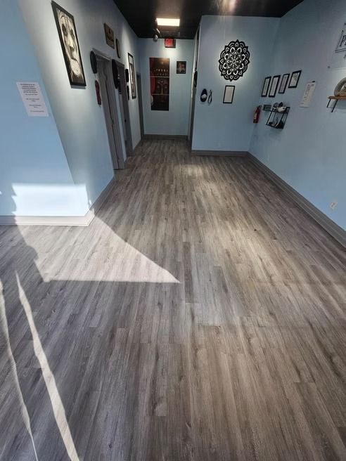 Long hallway with light blue walls, gray wood-look floor, framed art, and black ceiling.