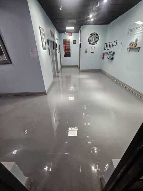 A hallway with glossy gray floor and light blue walls, art and doors.