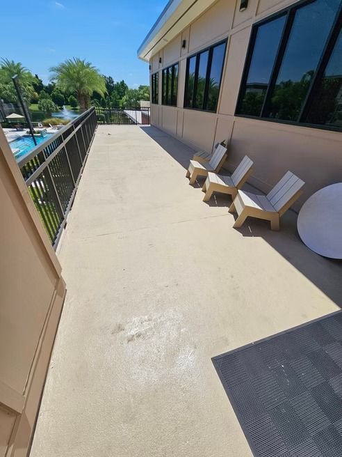 Tan concrete patio with metal railing, three chairs, and building with windows overlooking a pool.