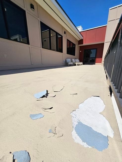 Exterior concrete patio with peeling paint near a building, sunny day.