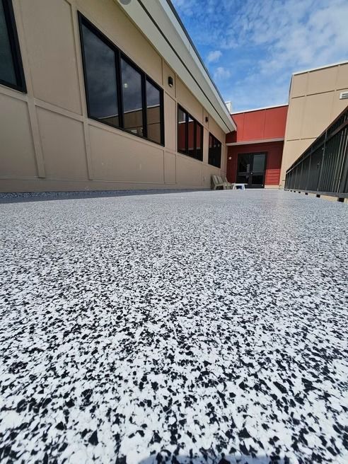 Exterior with speckled floor, tan wall, black windows, blue sky.