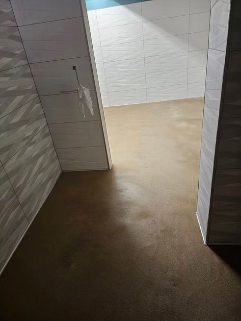 Bathroom with brown floor, white tiled walls. Open doorway leads to another room.