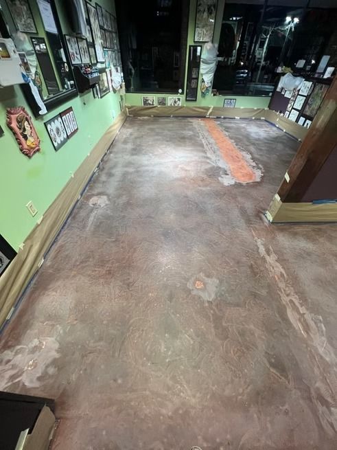 Bare, mottled concrete floor in a commercial space, with green walls and wooden trim.