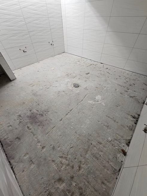 Empty room with rough concrete floor, white tiled walls.