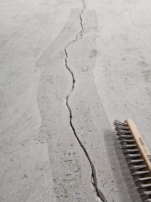 Crack in concrete floor with a wire brush to the side.