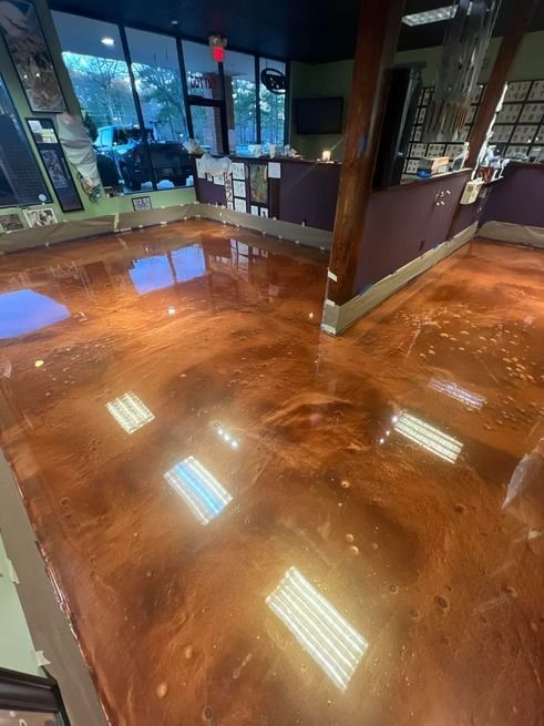 Shiny copper-colored epoxy floor in a business. Reflects overhead lights and a counter with dark purple walls.