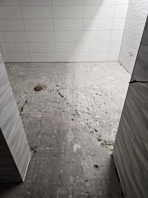 Empty bathroom with concrete floor, walls tiled white.