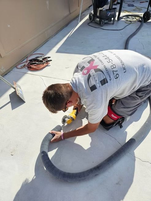 A person kneeling and using a tool, with a hose connected, on a concrete surface.