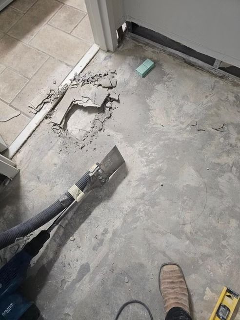 Concrete floor being chipped away near a door frame, with a vacuum hose and debris visible.