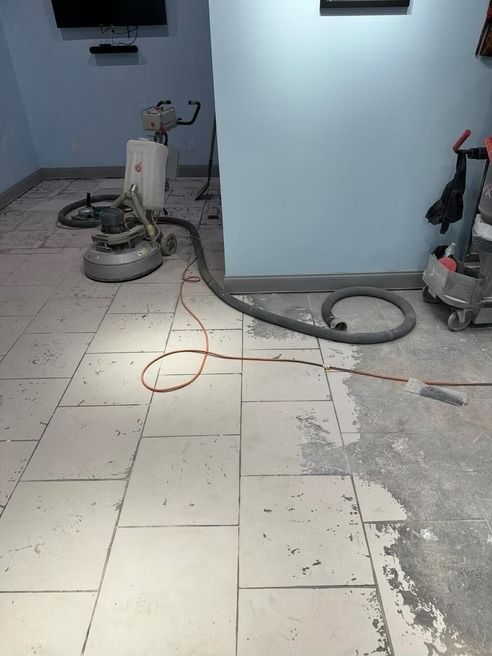 Floor sanding equipment in use, showing a room with partially sanded tile flooring and blue walls.