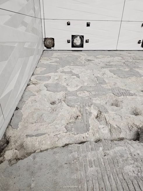 Uneven, gray concrete floor in a room with white tiled walls, possibly under construction.