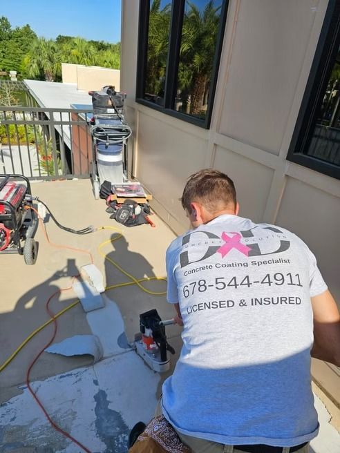 Man working on concrete, wearing a shirt with a logo and phone number. Outdoor setting.