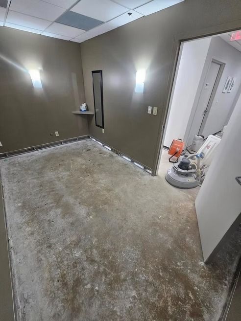 Room under construction: tan walls, unfinished floor, open doorway, floor grinder.