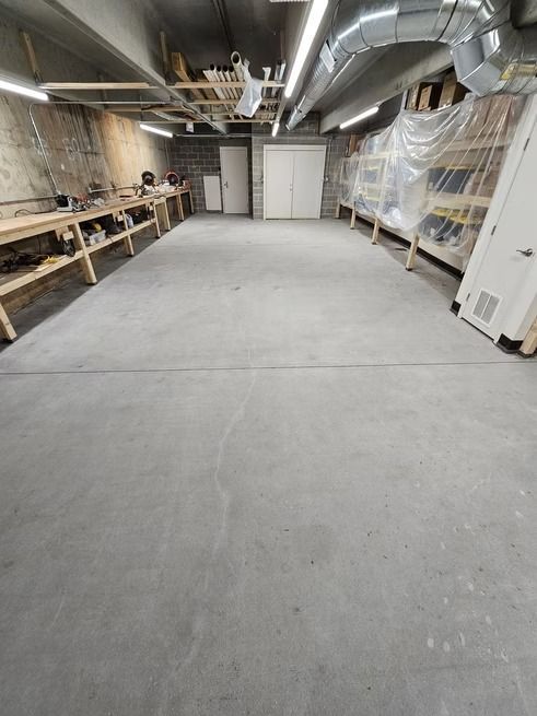 Concrete-floored basement workshop with workbenches on sides, storage shelves, and overhead lighting.