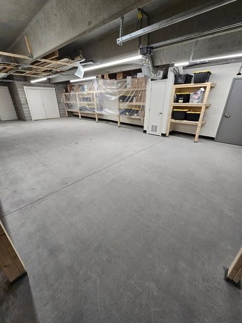 A basement with concrete floor, wooden shelving with items, and a white cabinet.