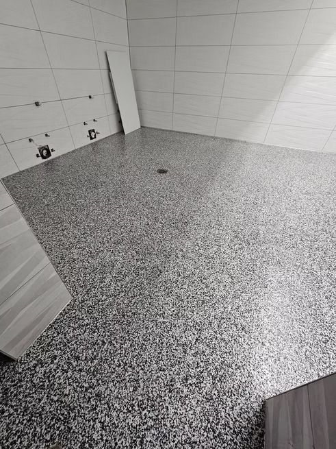 Bathroom with speckled gray floor, white tiled walls, and construction materials.