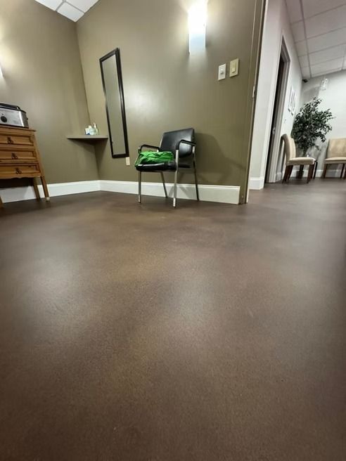 Waiting room with brown floor, olive walls, chair, and a narrow mirror.