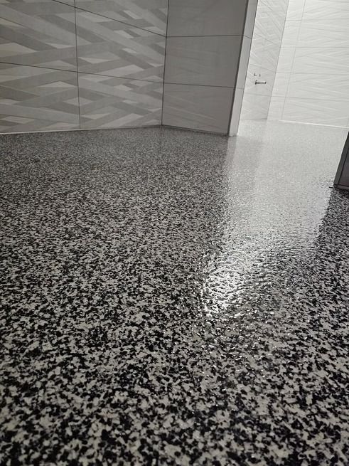 Gray and black speckled epoxy floor in a bathroom, reflecting light.