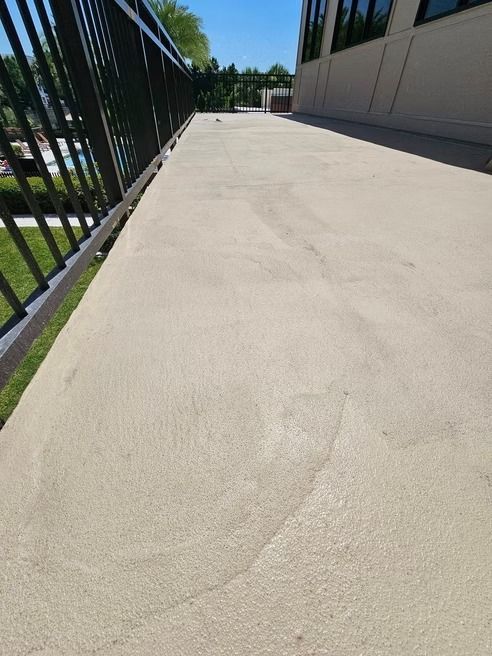 Concrete patio with a black railing and building in the background.