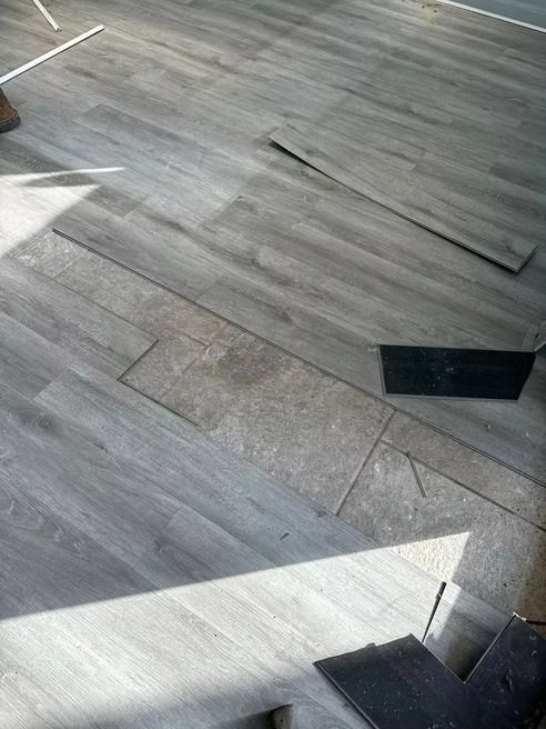 Gray wooden floor planks partially installed, with pieces scattered nearby.