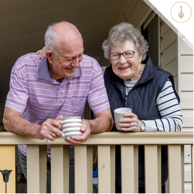 Older couple smiling while resting on a railing with coffee cups