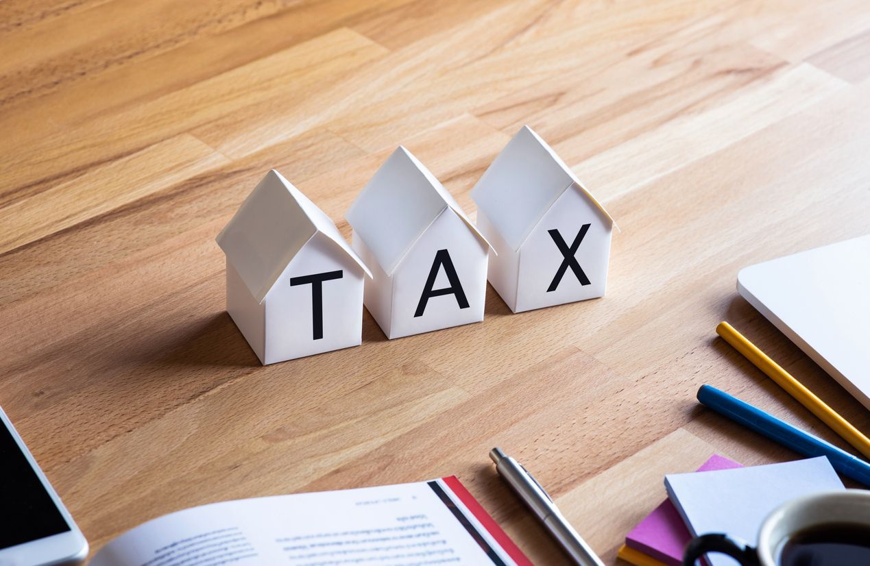 The word tax is written on a wooden table with small houses.