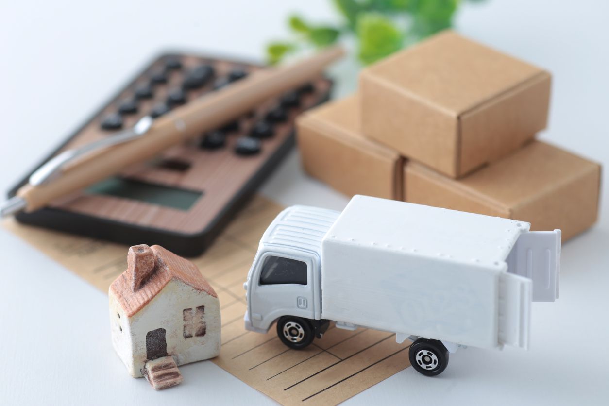 Miniature house, truck, boxes, calculator, and pen on a surface; symbolizing moving and financial aspects.