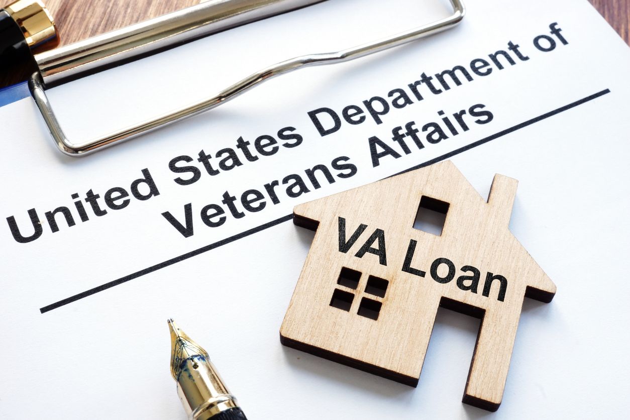 VA loan document with small wooden house, pen, and clipboard.