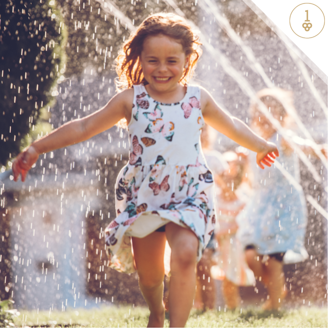 a little girl in a floral dress is running through a sprinkler.