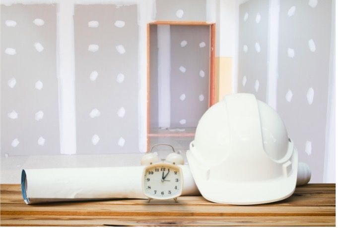 Hard hat, clock, and rolled up plans in a room under construction