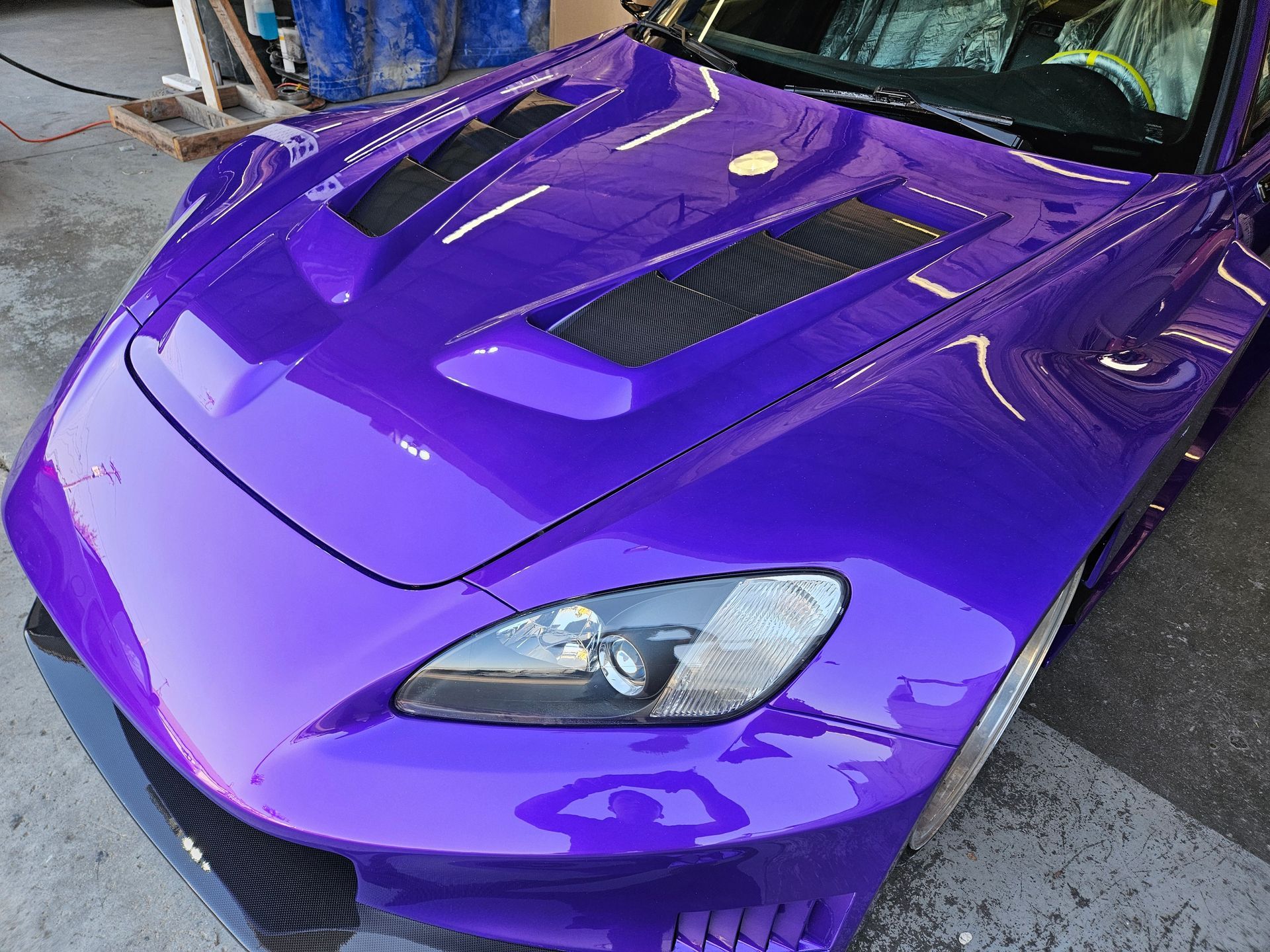 A purple car with a black hood is parked in a garage