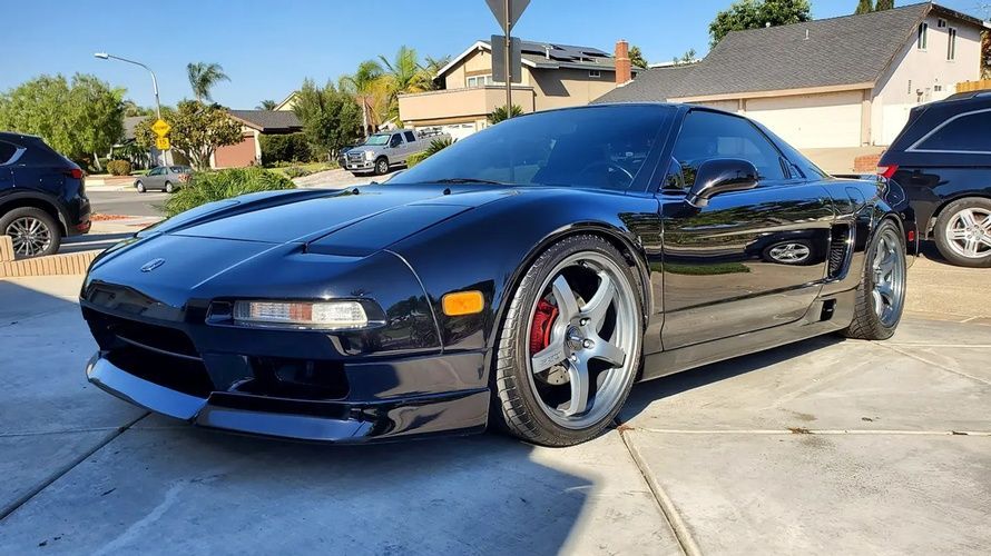 A black sports car is parked in a driveway in front of a house.