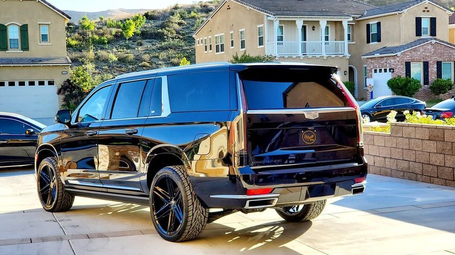 A black cadillac escalade is parked in a driveway in front of a house.
