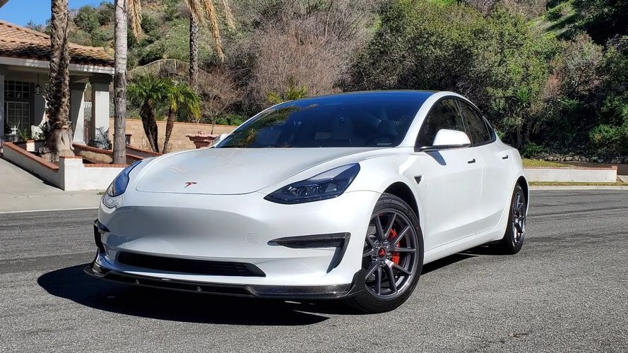 A white tesla model 3 is parked on the side of the road.