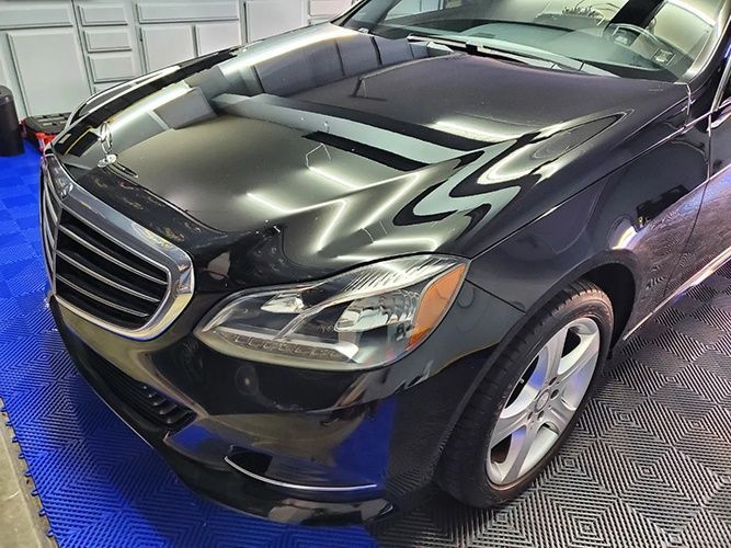 A black mercedes benz cls is parked on a blue mat in a garage.