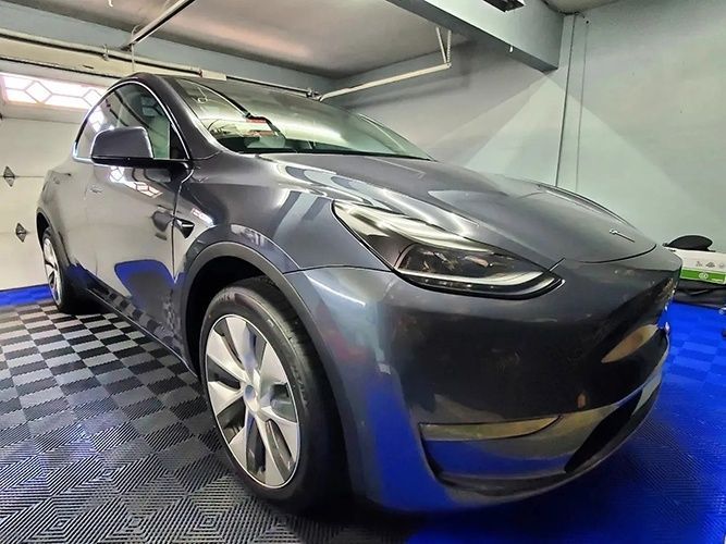 A tesla model y is parked in a garage on a checkered floor.