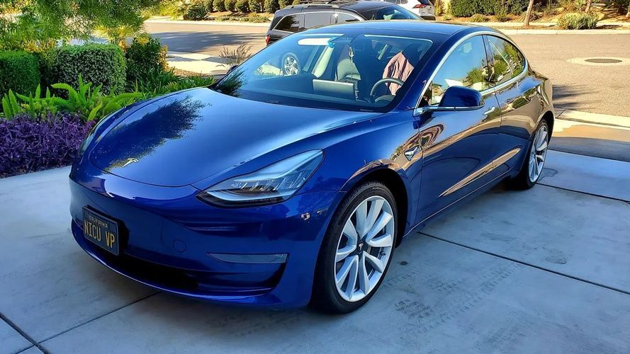 A blue tesla model 3 is parked in a driveway.
