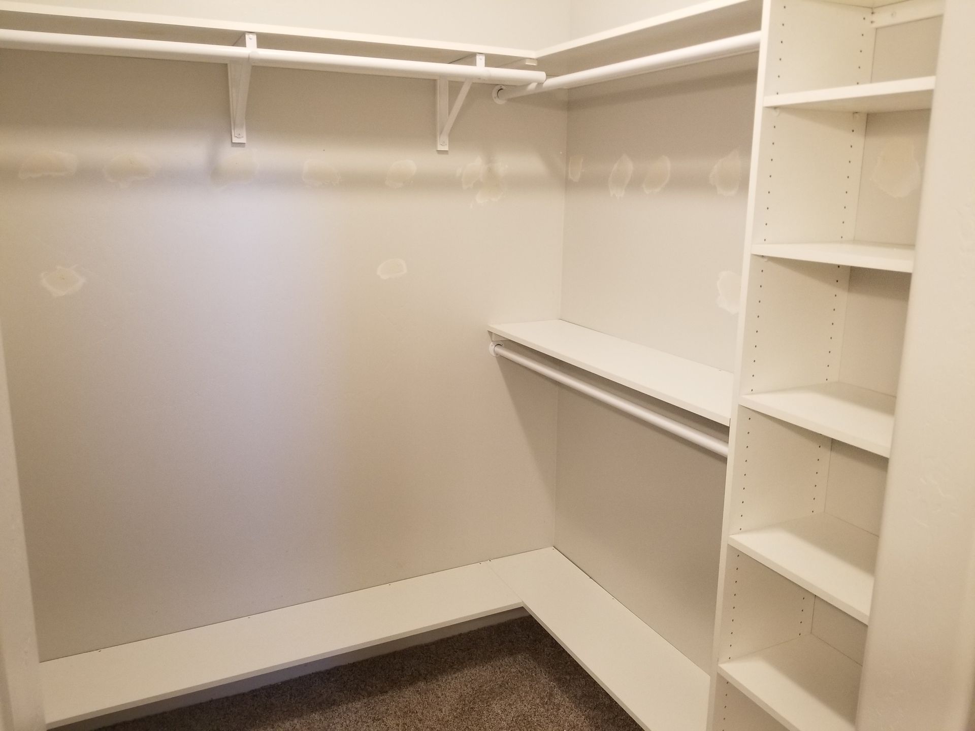 A walk in closet with white shelves and clothes racks.