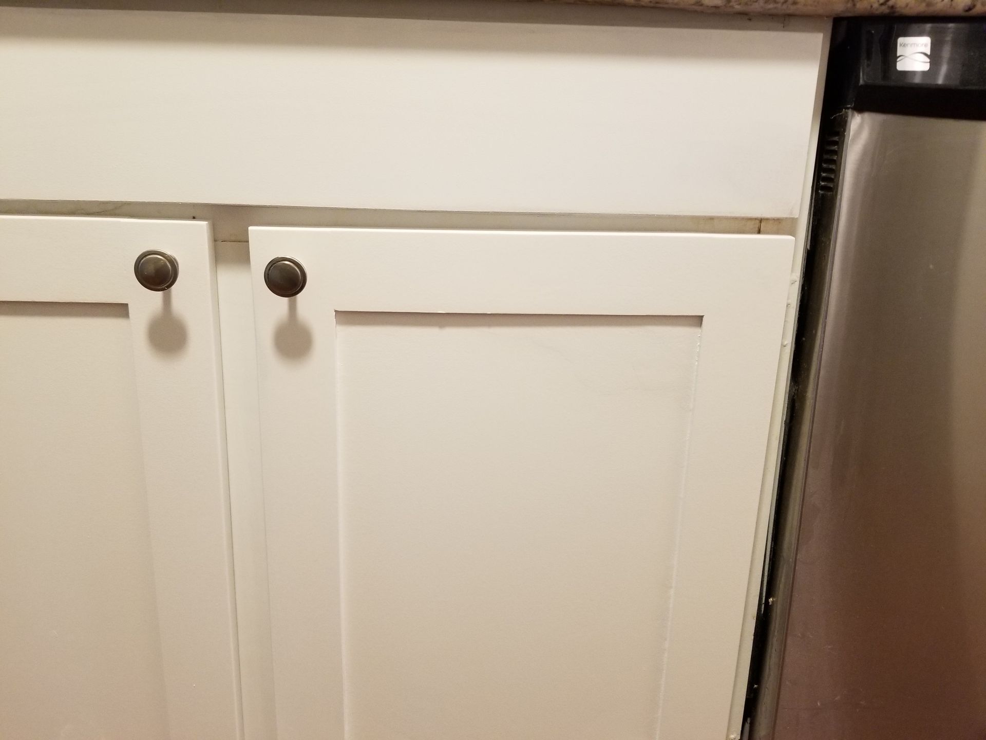 A kitchen sink with white cabinets and a stainless steel dishwasher.