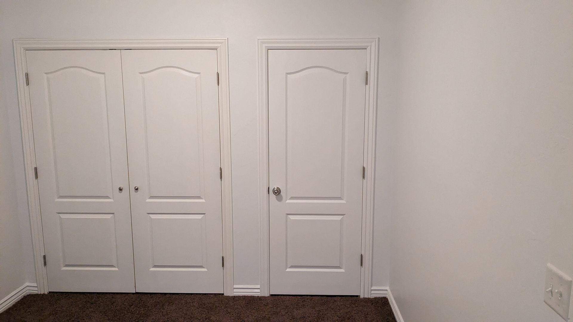 A room with two white doors and a brown carpet.