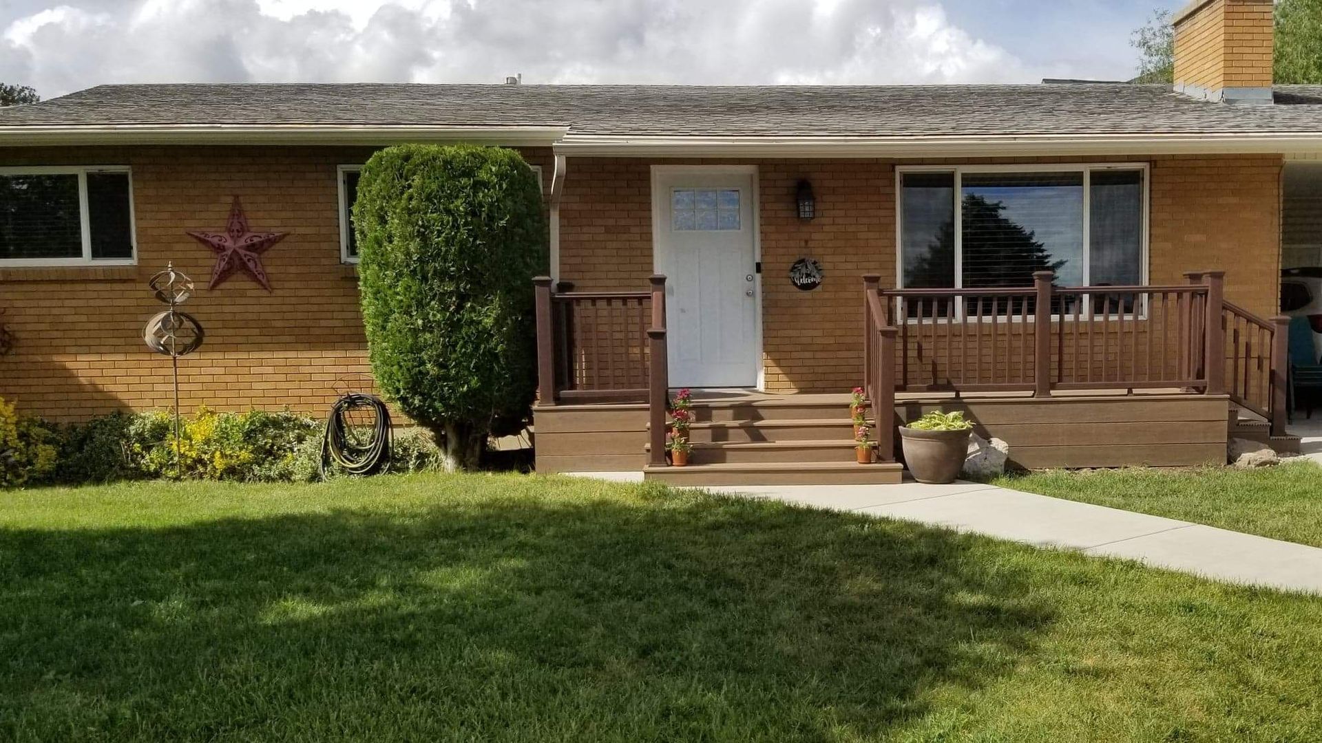 A brick house with a porch and stairs is sitting on top of a lush green lawn.