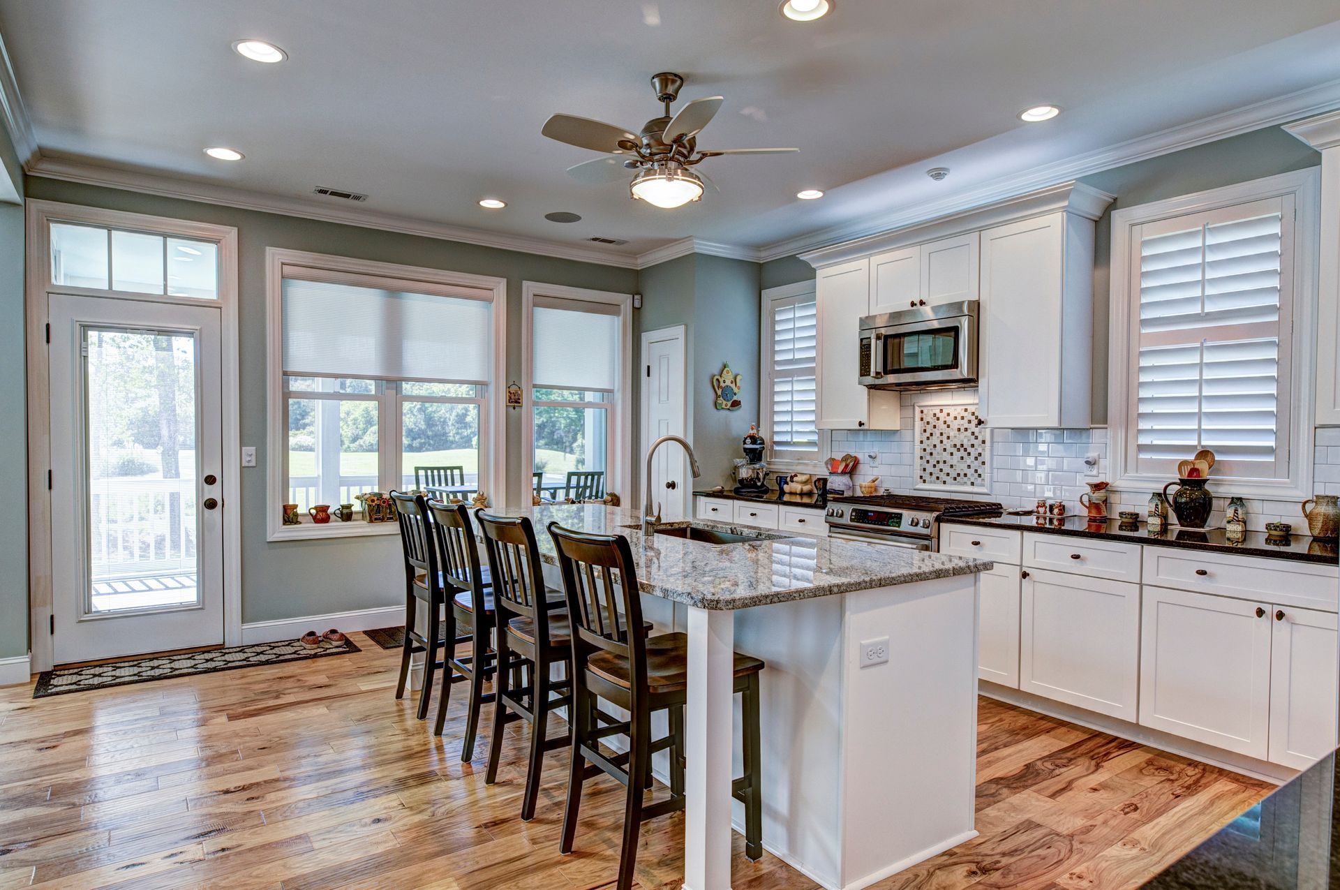 A kitchen with white cabinets , granite counter tops , stainless steel appliances and a ceiling fan.