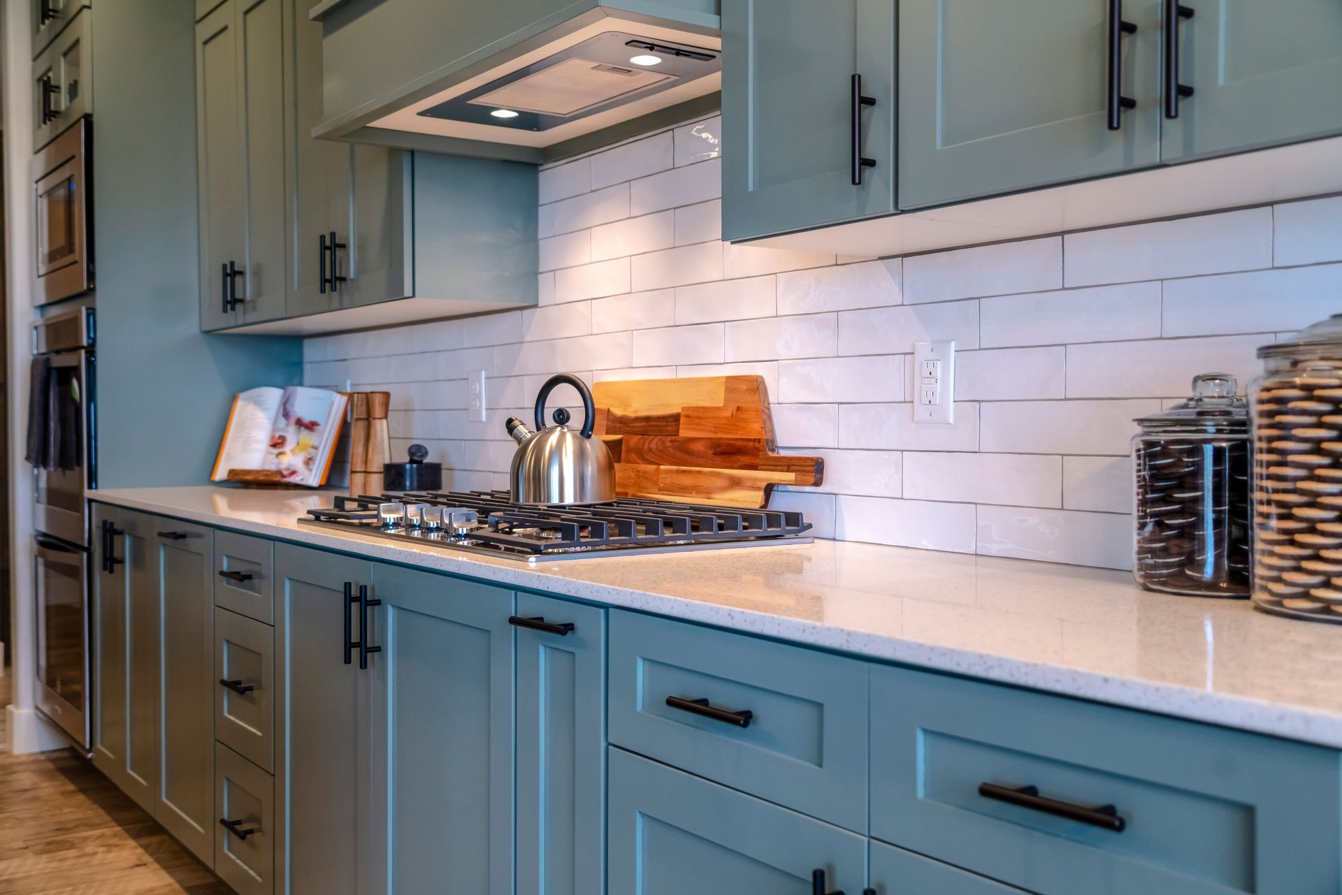 A kitchen with blue cabinets , white counter tops , and a stove top oven.