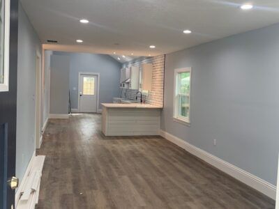 A living room with hardwood floors and a kitchen in the background.