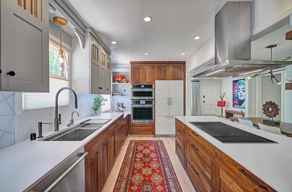 A kitchen with stainless steel appliances , wooden cabinets , white counter tops and a rug.