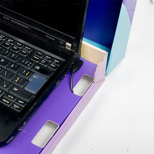 מחשב נייד מונח בתוך מעמד תצוגה מקרטון סגול וכחול עם חתכים ליד הפתחים הצדדיים.