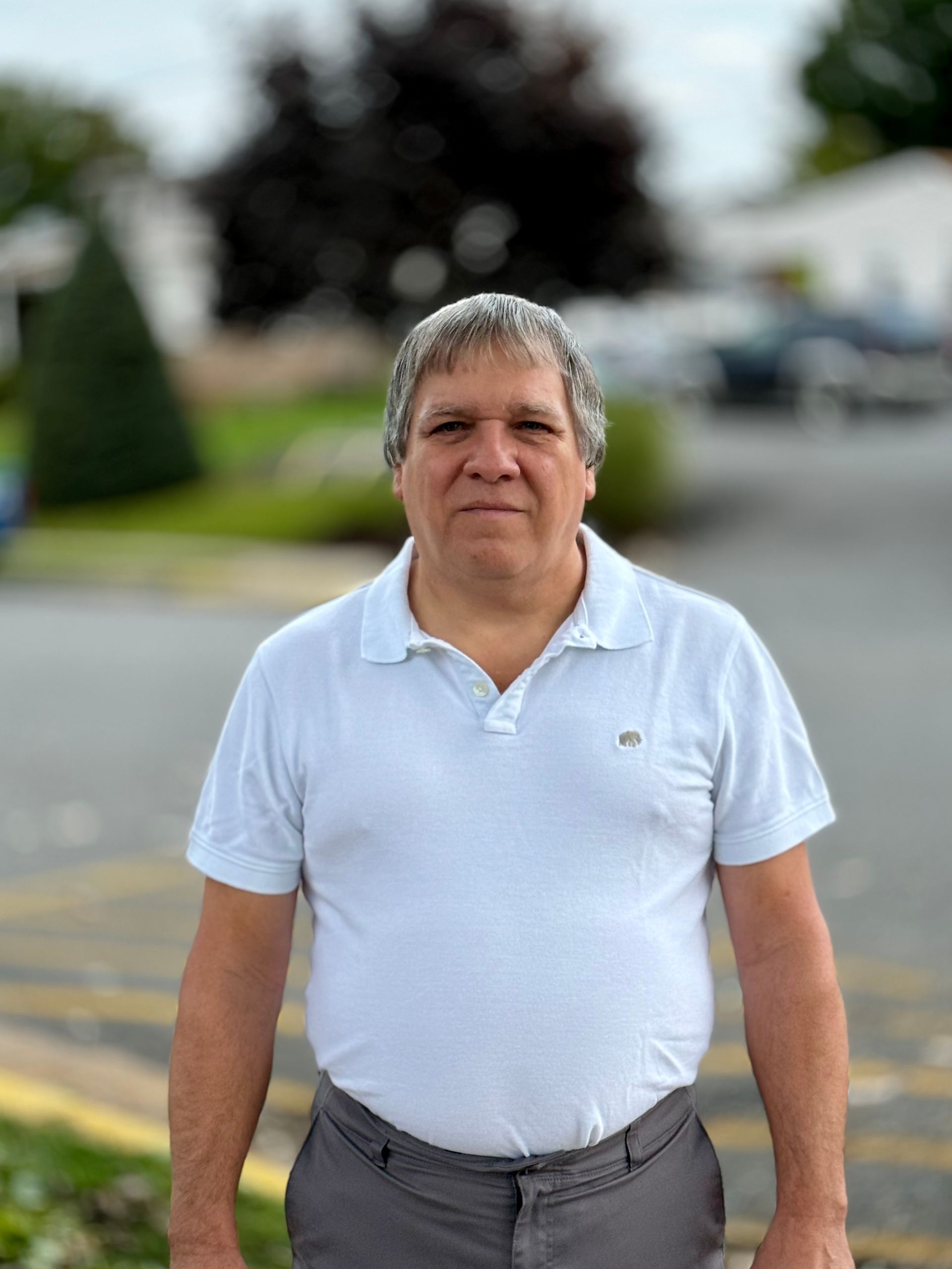 A man in a white shirt and gray pants is standing in a parking lot.