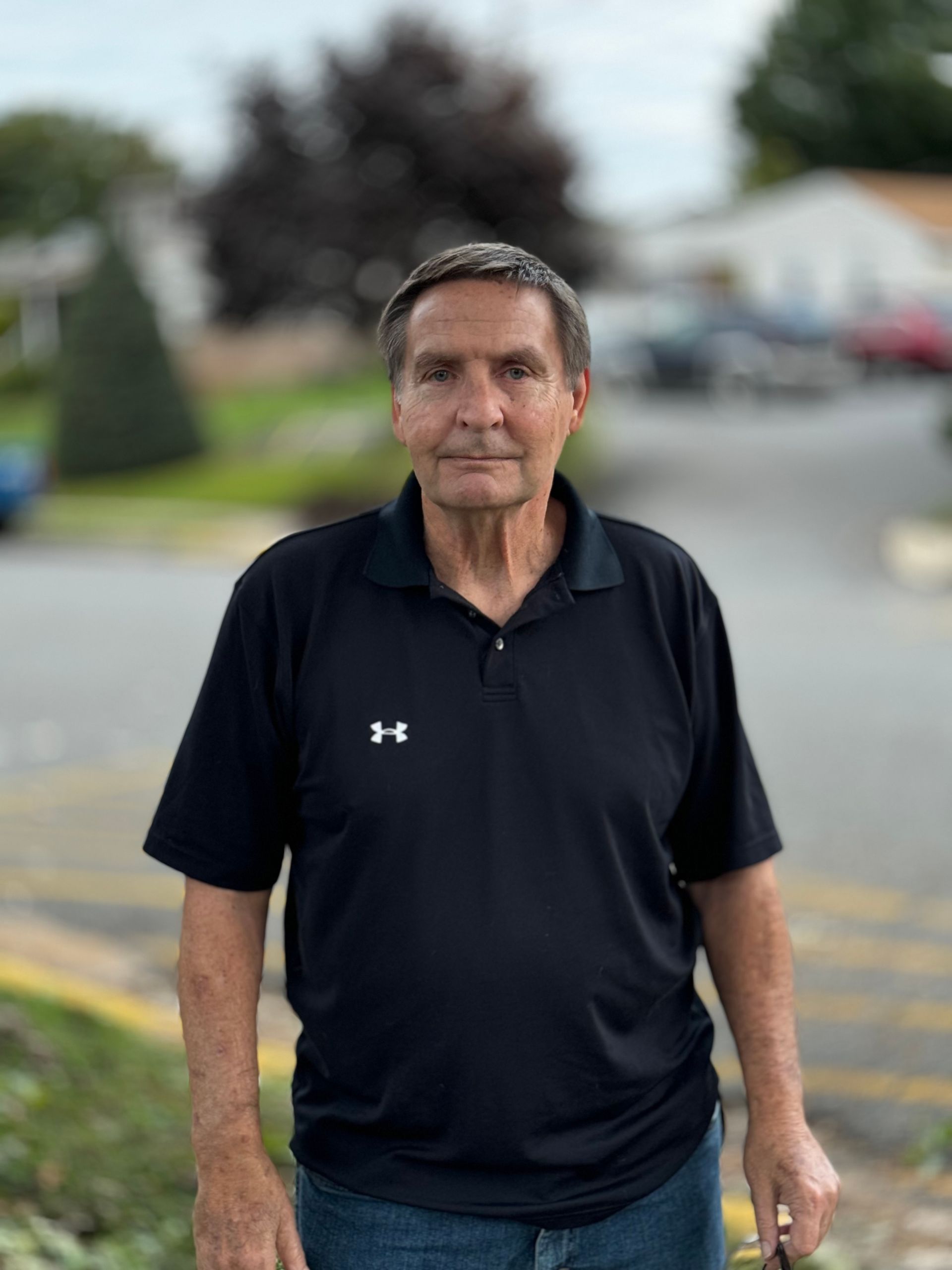 A man wearing a black under armour polo shirt is standing in a parking lot.