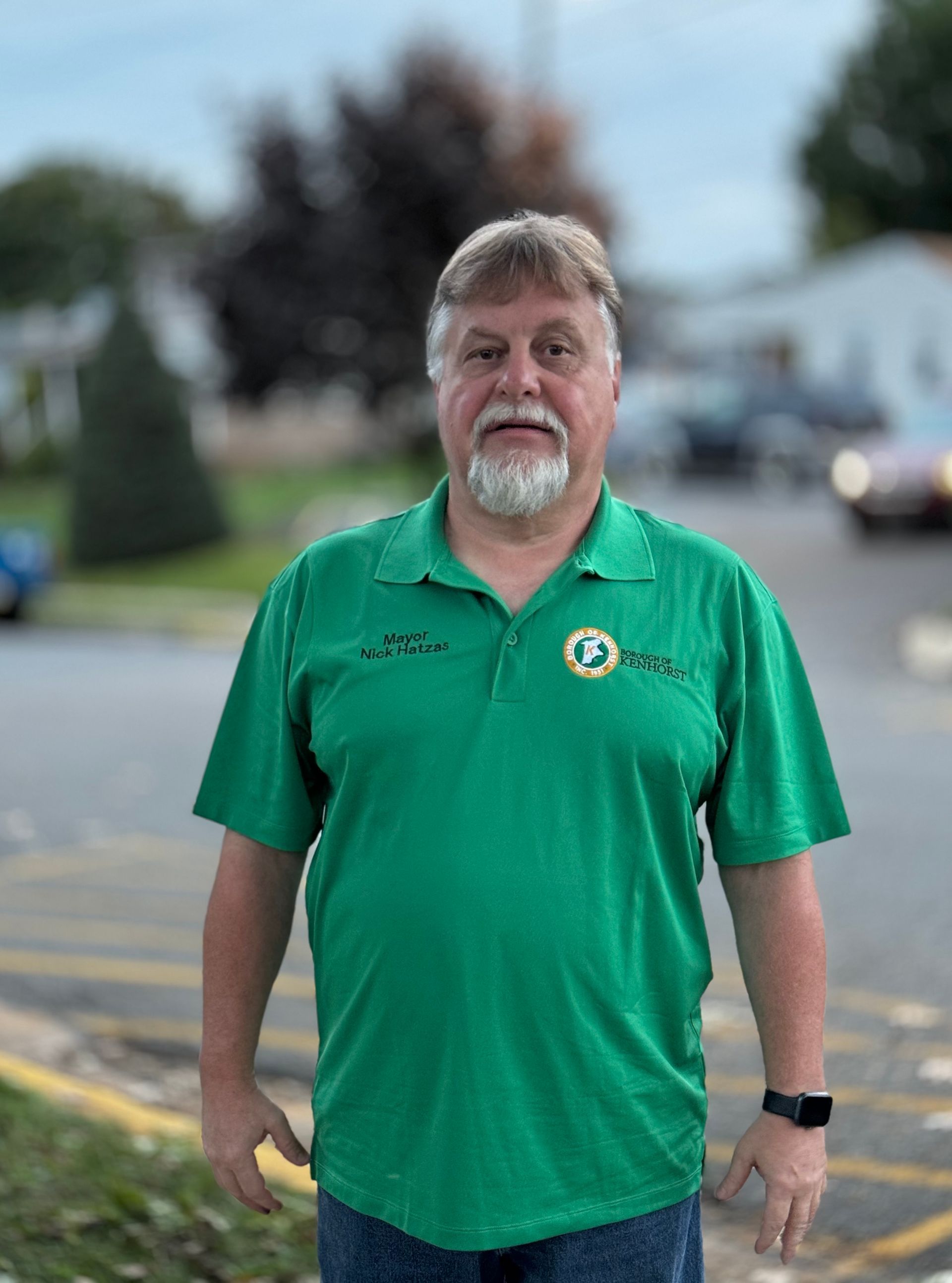 A man with a beard wearing a green shirt is standing in a parking lot.
